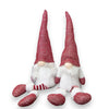 Two Christmas gonk gnomes seated on a white surface, showcasing their whimsical attire and cheerful expressions in a bright setting.