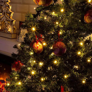 A beautifully decorated Christmas tree with led warm white Christmas lights and colourful ornaments stand beside a cozy fireplace, creating a festive atmosphere.